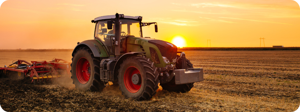 a green tractor harvesting with the sun in the background